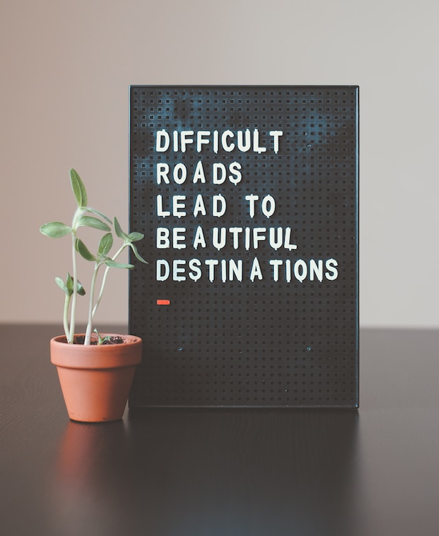 potted plant next to letter board that says, "Difficult roads lead to beautiful destinations"